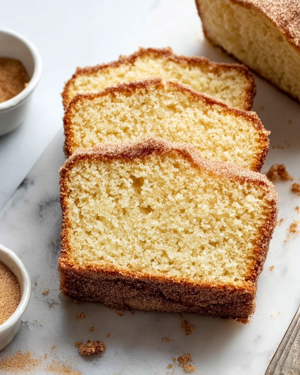 The image shows three slices of soft, golden yellow cake with a fine crumb texture, stacked slightly overlapping on a white marbled surface. The cake has a light brown crust with a sugar and cinnamon coating that adds a rough, grainy texture on the top and edges. There are some crumbs scattered around the slices. A small white bowl of cinnamon sugar is partially visible on the left side of the image. Photo taken with an iphone --ar 4:5 --v 7