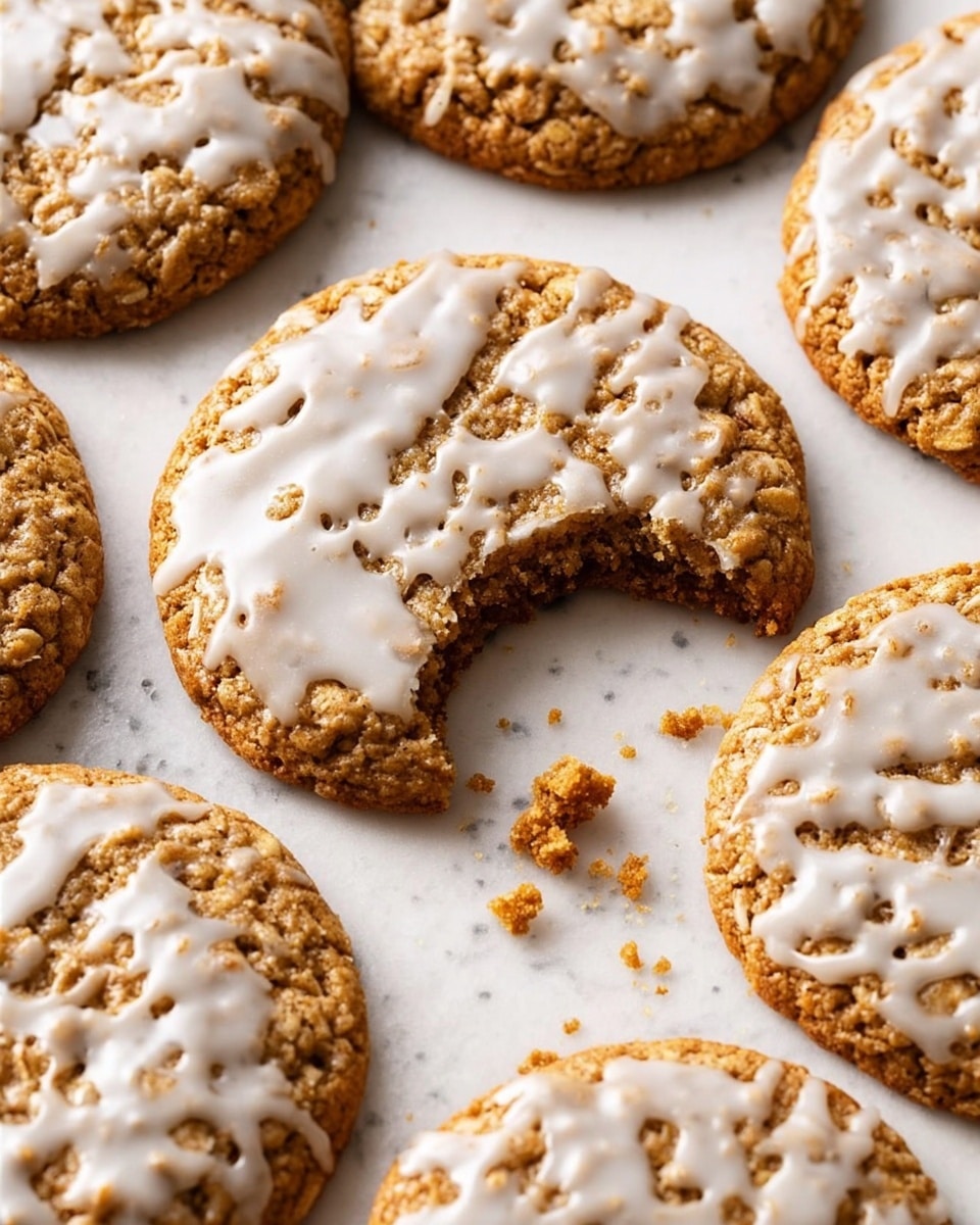 The image shows several round oatmeal cookies laid out on a white marbled surface. Each cookie is golden brown with a somewhat rough and bumpy texture from the oats. On top of each cookie, there is a white glaze spread unevenly, giving a soft, shiny contrast to the crunchy cookie below. One cookie in the center front has a bite taken out of it, revealing a slightly chewy and dense inside. Small cookie crumbs are scattered near this bitten cookie, adding a casual feel to the scene. The overall look is warm and inviting, with natural light highlighting the texture and shine of the glaze. photo taken with an iphone --ar 4:5 --v 7