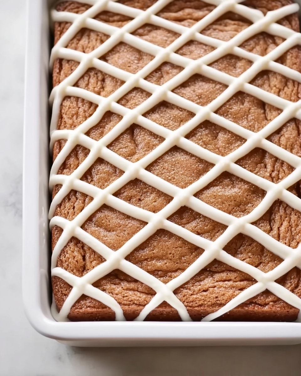 A rectangular baked dessert with a light brown, slightly textured top layer that appears soft and spongy. On top, there is a thick lattice pattern made of white icing, forming diagonal lines that crisscross each other, evenly spaced across the surface. The dessert is placed inside a white baking dish with slightly raised edges, resting on a white marbled surface. photo taken with an iphone --ar 4:5 --v 7