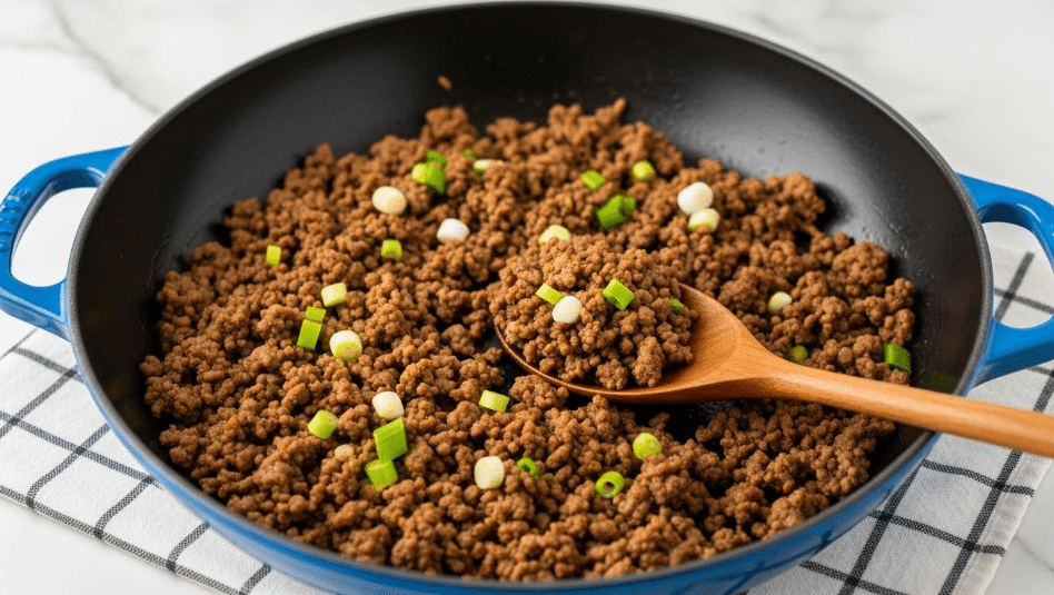 The image shows one layer of cooked ground meat mixed with small bits of green onions scattered on top, placed inside a dark blue cast iron pan with a smooth black inside surface. A wooden spoon with a rich brown color is resting inside the pan, lifting a portion of the meat mixture. The pan sits on a white marbled surface with a grid-like cloth underneath. The green onions add bright green spots of color among the rich brown of the cooked meat, giving texture and contrast. photo taken with an iphone --ar 4:5 --v 7