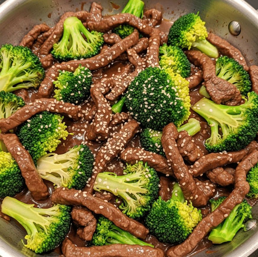 The dish shows a close-up view of a stir-fry in a silver pan filled with slices of brown cooked beef mixed with bright green broccoli florets. The beef pieces are glossy and coated in a thick dark brown sauce, while the broccoli has a fresh, slightly crisp look with some parts golden. Scattered lightly across the top are small white sesame seeds adding texture contrast. The ingredients are evenly mixed, filling the pan with a rich, vibrant combination of earthy and fresh colors. photo taken with an iphone --ar 4:5 --v 7