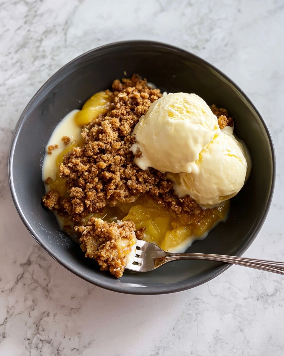 A white bowl holds a dessert with two main layers and a topping. The bottom layer is yellow and soft, looking like baked fruit. On top, there is a thick brown crumbly layer that has a rough texture with small oat pieces. Two pale cream-colored scoops of melting ice cream sit partly on the crumble and partly on the bowl, blending into the dessert. A fork is placed on the right side, digging into the dessert and holding a mix of the yellow base and brown crumble. The background is a white marbled surface. Photo taken with an iphone --ar 4:5 --v 7