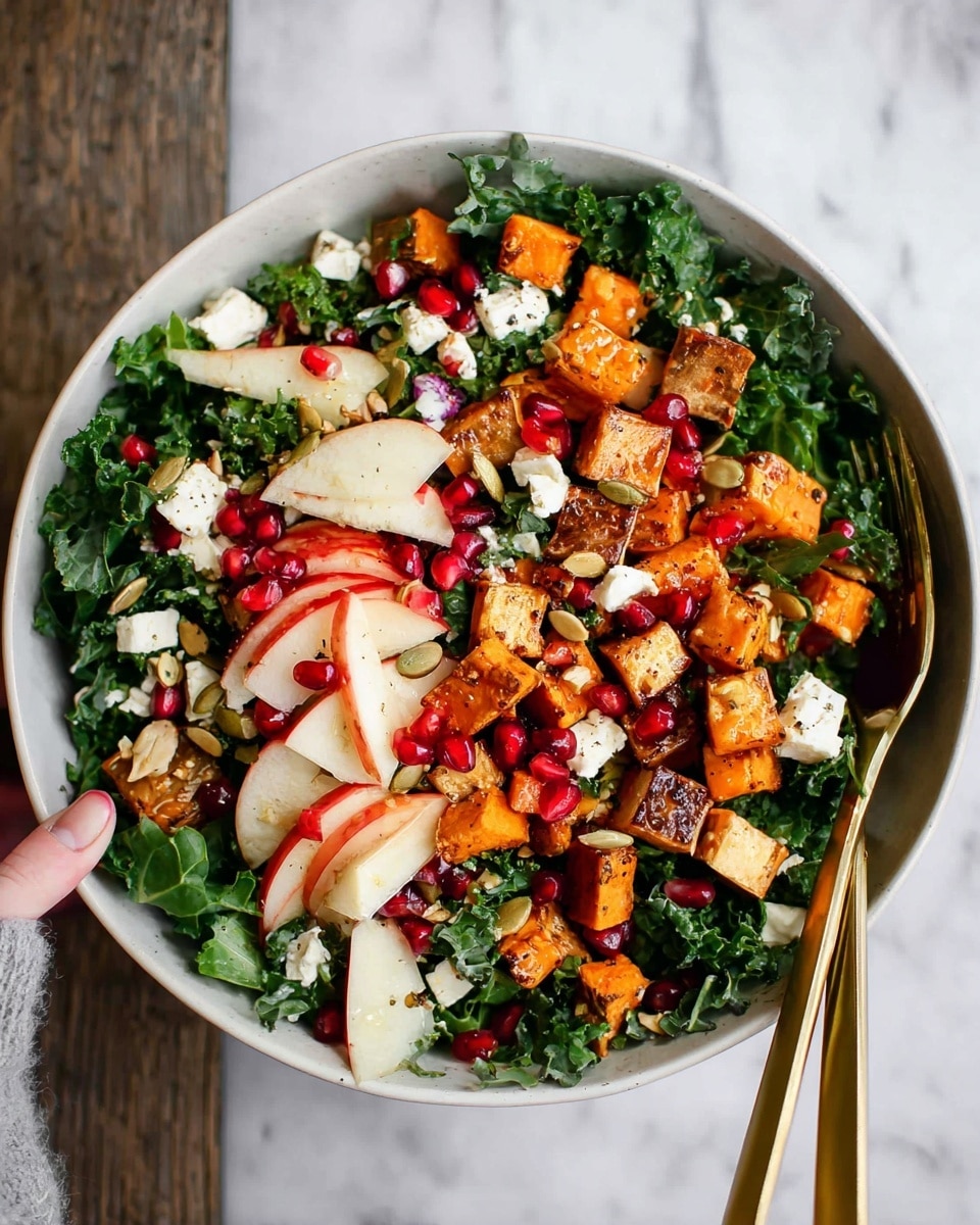 A white bowl filled with a colorful salad sits on a white marbled surface. The salad has three main layers: the bottom layer is dark green kale leaves with stems, creating a fresh and leafy base; the middle layer has orange roasted sweet potato cubes scattered evenly; the top layer includes small white cheese crumbles, bright red apple pieces with skin showing, and ruby red pomegranate seeds sprinkled throughout. There are also some toasted pumpkin seeds adding texture. Two gold forks rest inside the bowl, one held by a woman's hand. The photo is bright and clear with a natural look. photo taken with an iphone --ar 4:5 --v 7