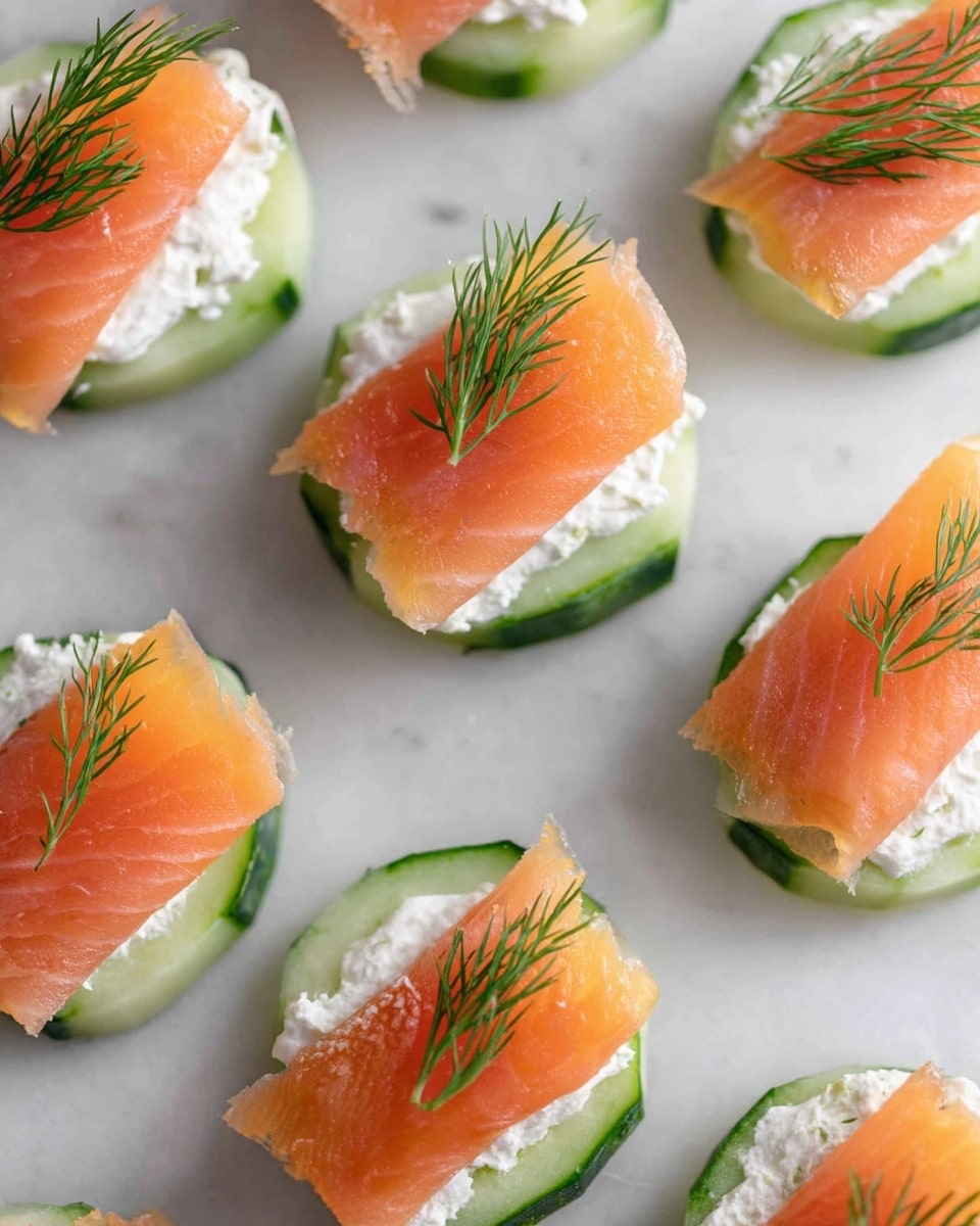 The image shows a white oval plate with several small round cucumber slices as the base layer. Each cucumber slice is topped with a thick layer of white cream cheese, smooth and slightly soft. On top of the cream cheese, there is a thin, folded light pink slice of smoked salmon, with a slightly shiny texture. Each piece is garnished with a small sprig of fresh green dill placed in the center. The plate is set on a white marbled surface, and a small white dish with extra dill is visible in the corner. Photo taken with an iphone --ar 4:5 --v 7