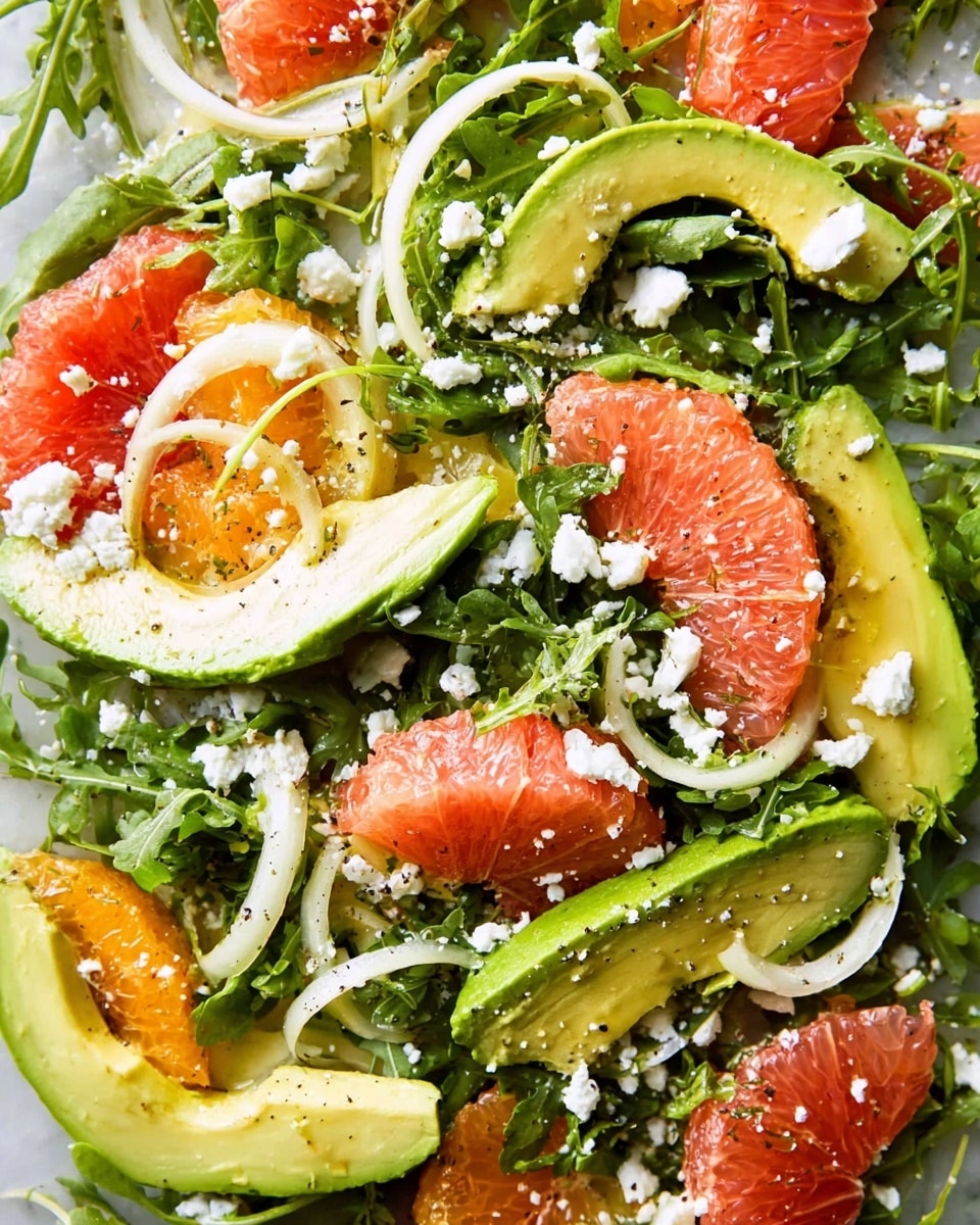 The image shows a fresh salad with a base layer of green arugula leaves that are slightly curly and textured. On top, there are several slices of creamy green avocado arranged in crescent shapes. Bright pink grapefruit and bright orange citrus segments add a pop of color, scattered evenly across the salad. Thin, pale white fennel slices lay around the fruit and avocado, adding a delicate touch. Crumbled white cheese is sprinkled over everything, adding a crumbly texture and contrast to the vibrant colors. The salad appears lightly dressed with a shiny, creamy dressing that glistens over the layers on a white marbled surface photo taken with an iphone --ar 4:5 --v 7