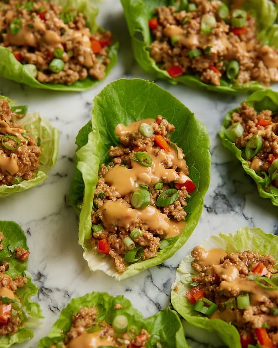 The image shows several crisp green lettuce leaves arranged neatly on a white marbled surface, each leaf holding a mixture of light brown ground meat, small red bell pepper pieces, and chopped green onions. The meat mixture is topped with a creamy, light tan sauce drizzled unevenly over the filling. The lettuce leaves are fresh and curved, creating a small bowl shape that holds the savory filling. The texture of the filling appears crumbly with a slight gloss from the sauce. photo taken with an iphone --ar 4:5 --v 7