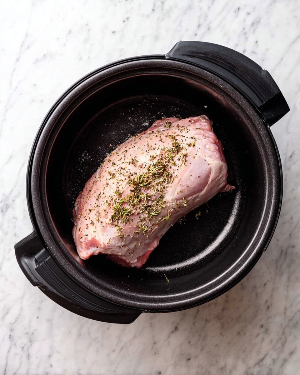 A large uncooked piece of meat, pale pink in color with some herbs sprinkled on top, rests inside a black cooking pot. The meat is positioned flat, showing a smooth texture with small bits of seasoning visible on the surface. The black pot has a rounded shape and strong handles on each side. The pot sits on a white marbled surface. photo taken with an iphone --ar 4:5 --v 7