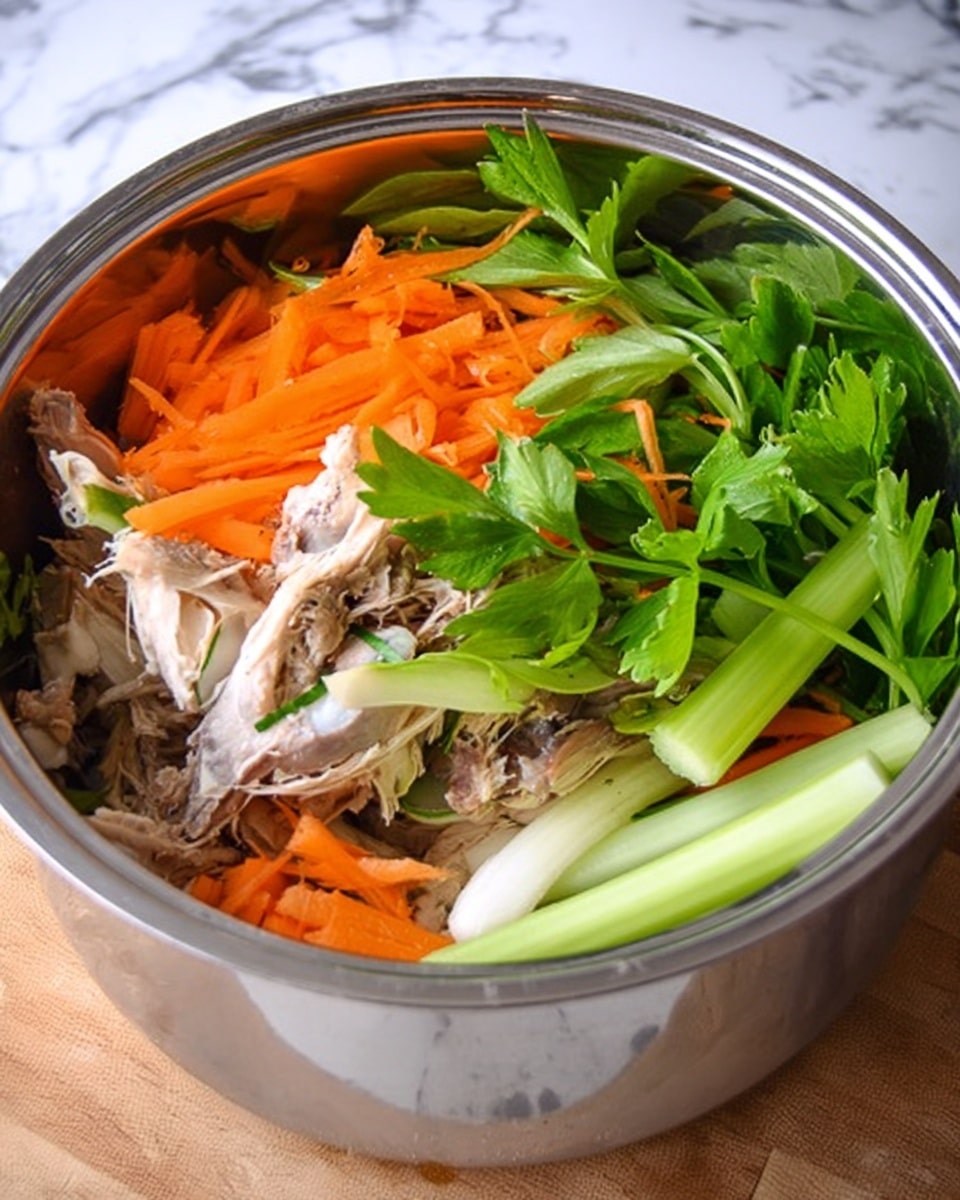 A shiny metal pot filled with several layers of ingredients: at the bottom, there are light brown cooked chicken bones; on top of that, bright orange shredded carrot layers are scattered unevenly; next, there are pale green celery stalks positioned in different directions, and some fresh bright green celery leaves rest on top, adding some height and color contrast. The pot is placed on a white marbled surface. photo taken with an iphone --ar 4:5 --v 7