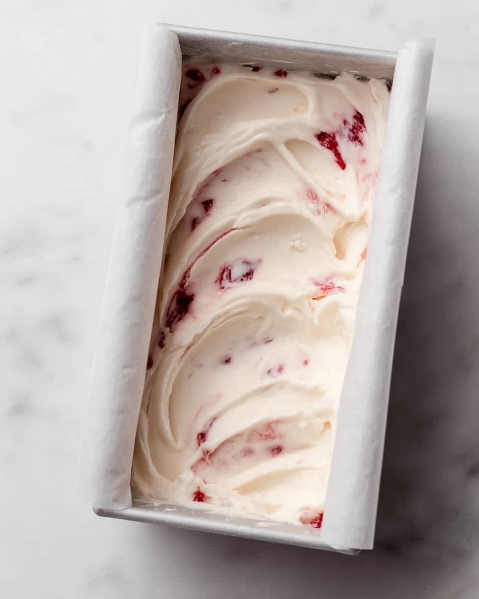 The image shows a metal rectangular container with remnants of creamy white ice cream mixed with red strawberry swirls inside. One scoop of the ice cream, rounded and smooth with a mix of white and red colors, is held by a metal ice cream scooper with a beige handle resting in the container. The container lies on a white cloth with blue stripes, placed on a white marbled surface. To the right of the container, there are two white bowls; the larger bowl holds bright red frozen strawberries, while the smaller bowl contains sliced light brown almonds. Behind the smaller bowl, there is a white cup with two light wooden spoons inside. The overall look is clean and bright with soft, natural light. photo taken with an iphone --ar 4:5 --v 7