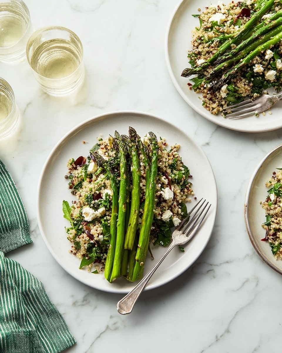 Two white plates sit on a white marbled surface, each holding a dish with two layers: the bottom layer is a mix of grains, chopped greens, and small chunks of white cheese, all mixed tightly with specks of dark red and green leaves, creating a colorful and textured base. On top, four grilled green asparagus spears are laid side by side, their slightly charred marks adding a rustic look. A silver fork rests beside the asparagus on each plate. A green and white striped cloth is partially visible in the top left corner, and two glasses with water or a clear liquid sit nearby. photo taken with an iphone --ar 4:5 --v 7