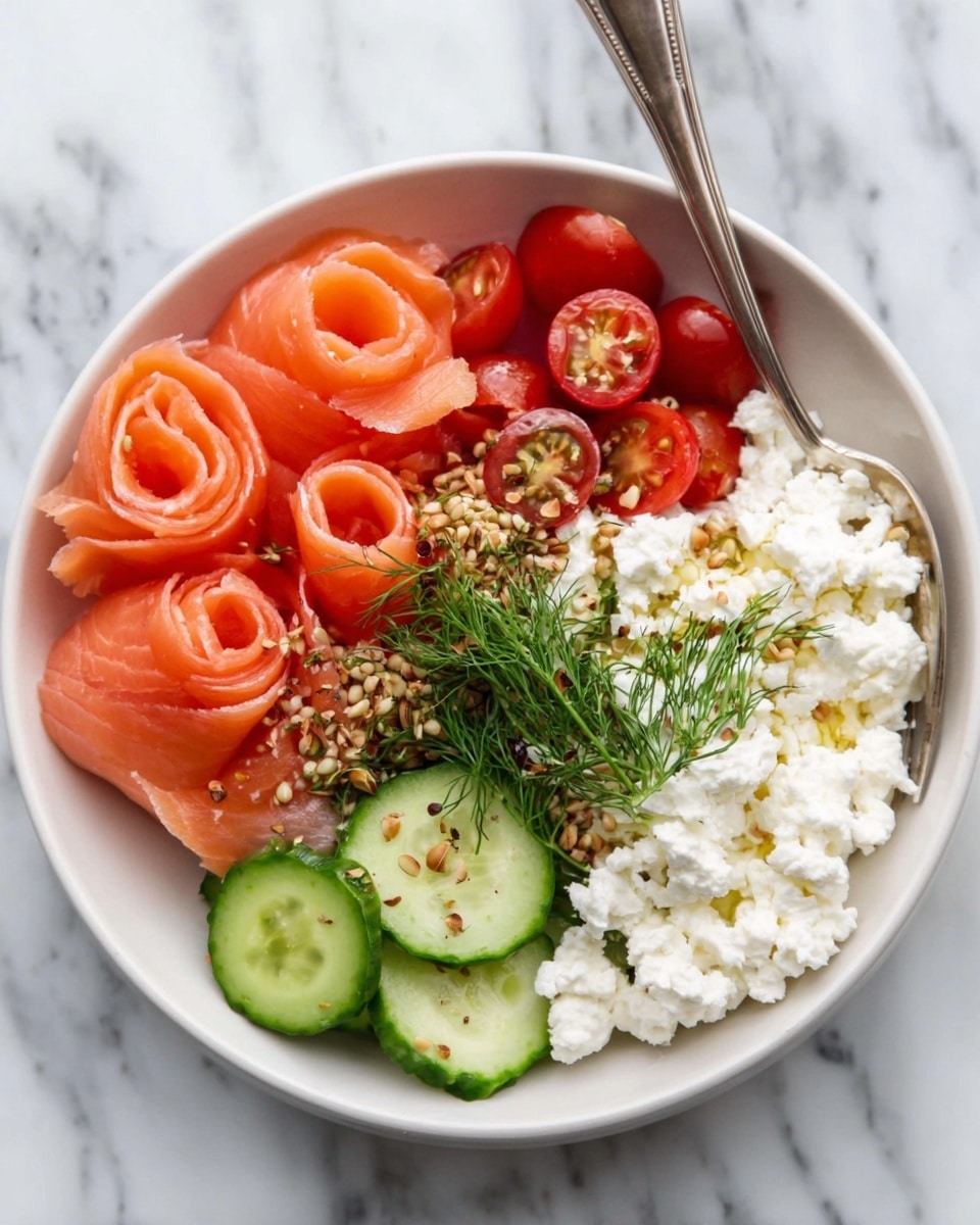 A white bowl filled with several layers: thinly rolled pink smoked salmon slices are arranged in a loose rose shape on one side; next to it are three slices of fresh green cucumber stacked slightly overlapping; a mound of white cottage cheese textured with small curds is placed beside the cucumber; half a dozen bright red cherry tomato halves lie close together near the cottage cheese; the dish is garnished with a small bunch of fresh green dill and sprinkled with chopped nuts or seeds over the tomatoes and salmon. A silver spoon rests inside the bowl on a white marbled surface. Photo taken with an iphone --ar 4:5 --v 7