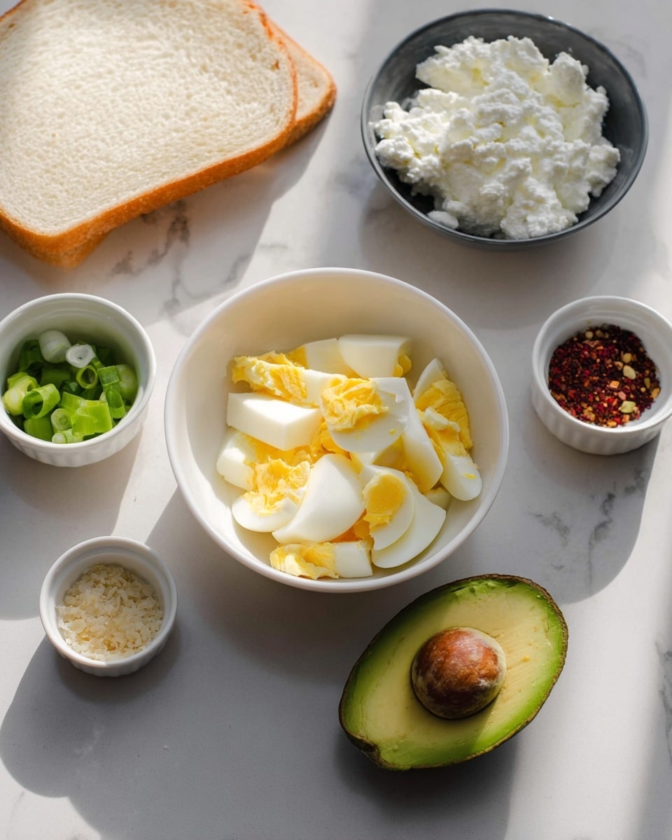 The image shows ingredients for a simple meal arranged on a white marbled surface. In the center, there is a white bowl with chopped hard-boiled eggs, showing layers of white and yellow pieces. To the top right, there is a dark bowl filled with white cottage cheese with a thick texture. Next to it is a small white ramekin holding a bit of red and black spices. Below, a halved avocado with bright green flesh and a brown seed rests on the surface. To the left of the center bowl, there is a small white ramekin with chopped green onions and another small white ramekin with a dollop of grainy mustard. In the background, a slice of light beige bread lies flat on the surface. The lighting is soft with a natural shadow cast from the bottom left. photo taken with an iphone --ar 4:5 --v 7