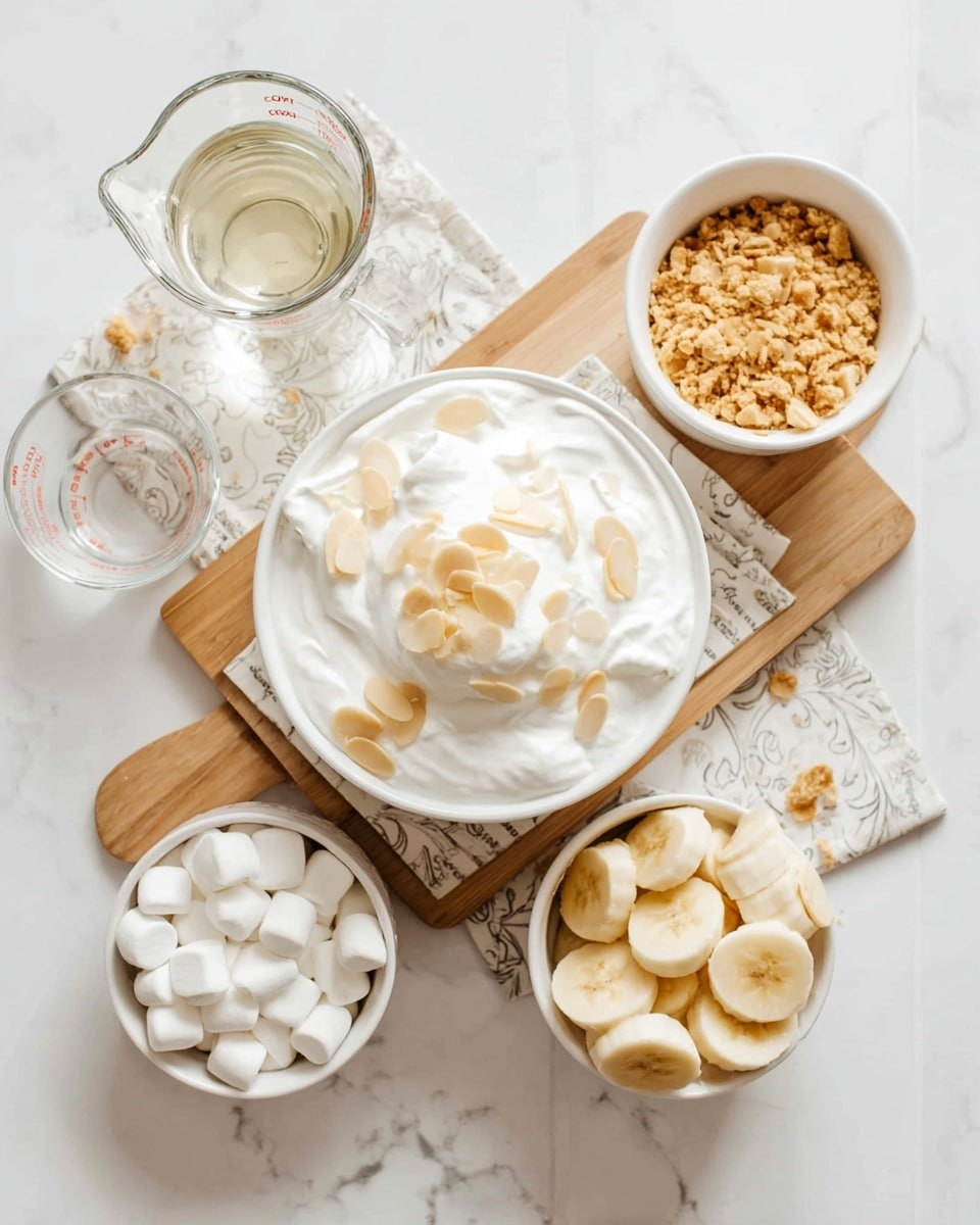 A top view of a dessert assembly on a white marbled surface, featuring a white bowl in the center with a thick layer of white whipped cream topped with small almond slices. Around the bowl, there is a round white dish with small white marshmallows at the bottom left, a white bowl with sliced bananas and bananas slices at the bottom right, and a white bowl filled with crushed cookie crumbs and some almond slices at the top right. To the left, a glass measuring cup filled with a clear liquid and an empty small white bowl complete the setting. The bowls and cups are arranged on a patterned cloth over a wooden cutting board. Photo taken with an iphone --ar 4:5 --v 7