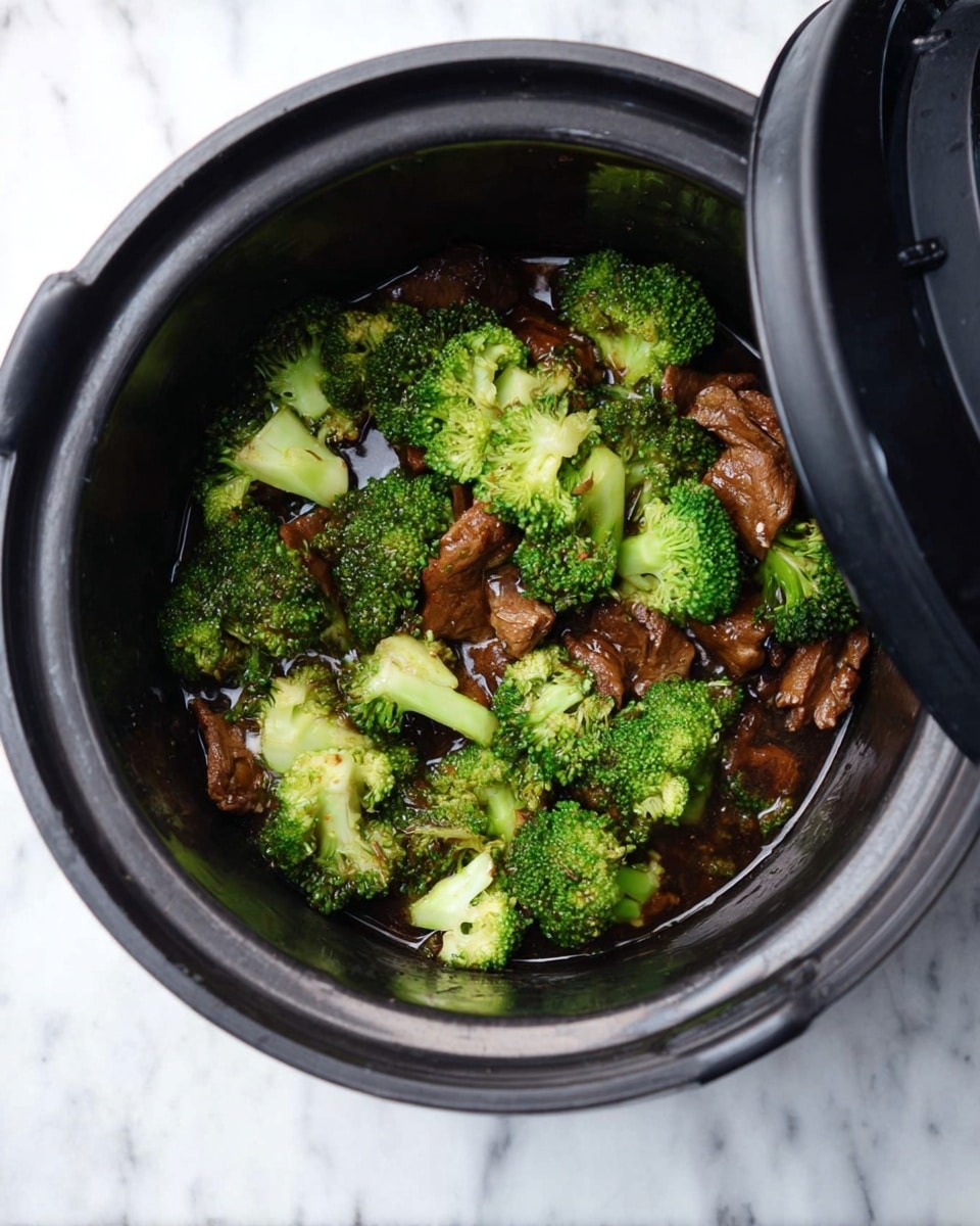 The image shows a close-up top view of a stainless steel pot filled with a mix of dark brown cooked beef strips and bright green broccoli florets, coated in a thick glossy sauce. The beef pieces are textured and look tender, spread evenly around the pot, with broccoli pieces scattered throughout, showing a fresh crisp look. The pot handles are black and the pot sits on a white marbled surface with a power cord visible on the side. photo taken with an iphone --ar 4:5 --v 7