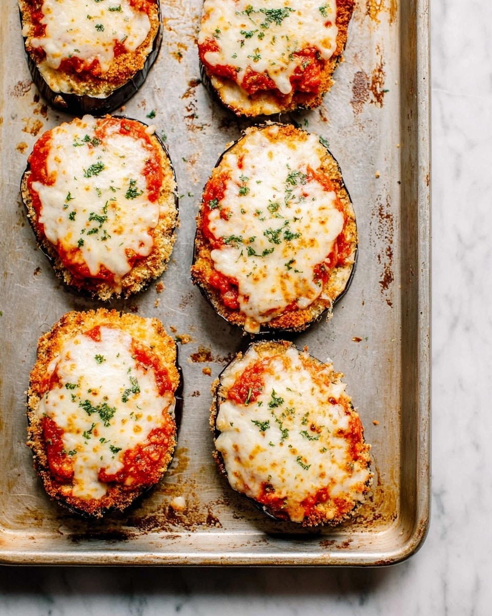 Six pieces of eggplant slices are placed on a silver baking tray with some browned crumbs around. Each slice has three layers: the bottom layer is a crispy golden-brown breaded eggplant, the middle layer is bright red tomato sauce with small bits visible, and the top layer is melted white cheese that is browned in spots giving a slightly bubbly texture. Small green parsley flakes are sprinkled evenly over the cheese for color. The tray rests on a white marbled surface. photo taken with an iphone --ar 4:5 --v 7
