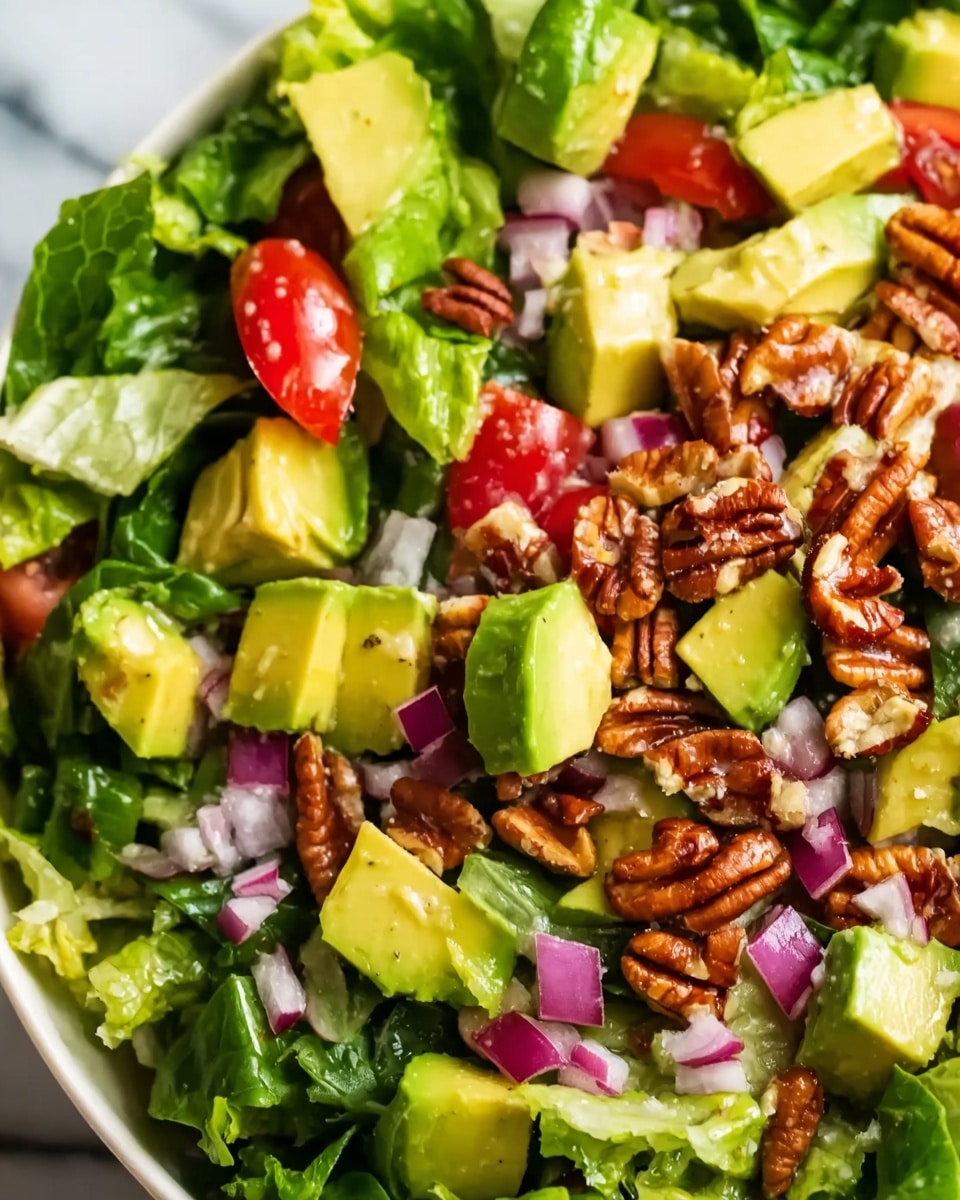 A close-up view of a fresh salad with several layers: at the bottom, there is a mix of green leafy lettuce; on top of the greens, there are chunks of bright yellow-green avocado evenly spread out; scattered among the avocado are small red tomato pieces with a juicy texture; diced purple-red onion pieces are also mixed in, adding contrast; the salad is topped with unevenly placed light brown pecan nuts, giving a crunchy texture. The salad is shown on a white plate set on a white marbled surface. Photo taken with an iphone --ar 4:5 --v 7
