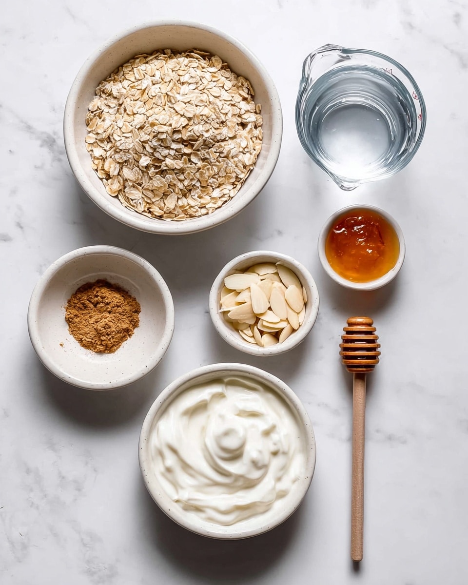 The image shows six small white bowls and a clear glass measuring cup arranged on a white marbled surface. The largest white bowl holds a heap of dry oats with a textured surface. Next to it, another white bowl contains smooth white yogurt with gentle swirls. A smaller white bowl has a light brown powder, likely cinnamon. Another small white bowl has sliced almonds with a rough, pale texture. There is a clear glass measuring cup filled with water. Near the top right, a small white bowl holds honey, slightly shiny with a golden amber color, and next to it lies a wooden honey dipper with smooth rounded ridges. photo taken with an iphone --ar 4:5 --v 7