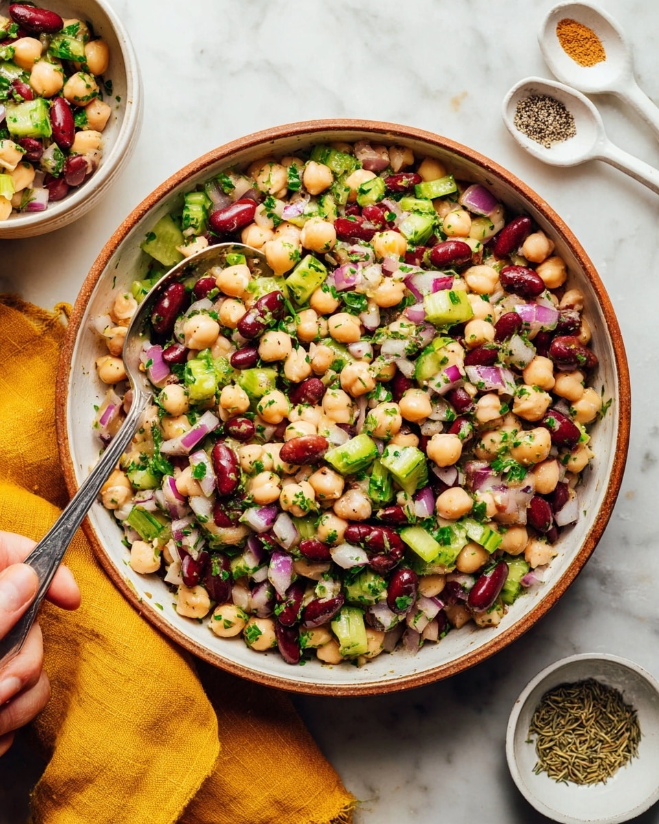 A bowl of mixed bean salad with three layers: the first layer has light beige chickpeas, dark red kidney beans, and white beans, all round and smooth; the second layer is chopped bright green celery and small pieces of purple-red onion, adding freshness and crunch; the final layer is scattered fresh green parsley leaves and bits of black pepper sprinkled on top. The salad is in a deep white bowl with a brown rim, placed on a white marbled surface, with two vintage silver spoons inside the bowl. Around the bowl, there are fresh green parsley sprigs on a white marbled surface, white spoons with salt and spices, and a soft mustard yellow cloth. Photo taken with an iphone --ar 4:5 --v 7