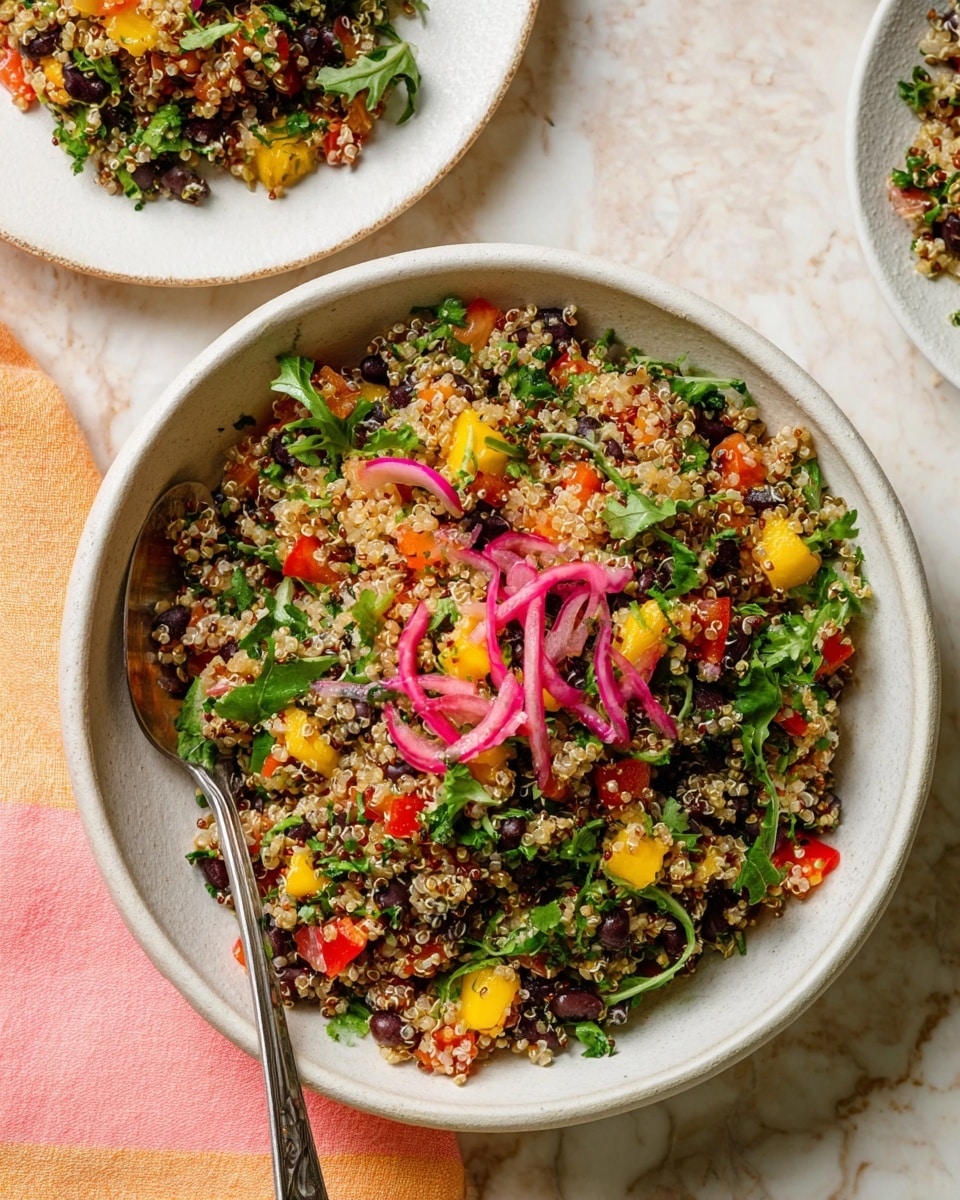A white ceramic bowl filled with a colorful quinoa salad, showing at least six visible layers of ingredients mixed together: small light beige quinoa grains, red diced bell peppers, black beans, bright green chopped parsley and arugula leaves, yellow chunks of mango, and thin pink pickled onion slices scattered on top. The salad looks fresh with a mix of soft and crunchy textures. There is a silver spoon partially inserted on the left side of the bowl. The bowl is placed on a white marbled surface with a pastel pink and orange striped cloth nearby. Another white plate with a smaller portion of the salad is visible in the top left corner. Photo taken with an iphone --ar 4:5 --v 7
