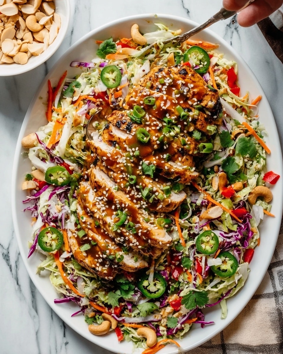 The dish shows a white oval plate filled with shredded cabbage and carrot salad mixed with sliced red bell peppers and purple cabbage as the base layer. On top are two rows of grilled sliced chicken, golden brown with visible grill marks. The chicken is garnished with chopped green onions, fresh cilantro, sliced jalapeño rings, sesame seeds, cashews, and almond slivers, creating a colorful and textured look. The plate is set on a white marbled surface with scattered herbs and nuts around. A large metal spoon rests on the right side of the plate. Photo taken with an iphone --ar 4:5 --v 7