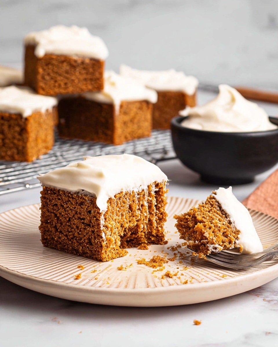 A slice of crumbly orange cake sits in the center of a light beige plate with a textured surface, topped with a dollop of white cream sprinkled lightly with a reddish powder. Behind the main slice, there are four more orange cake squares stacked on a metal cooling rack against a white marbled background. To the right, a small black bowl filled with more white cream is partially visible, with a silver spoon nearby. The overall look is warm and inviting, focusing on the texture of the cake and the smooth cream on top photo taken with an iphone --ar 4:5 --v 7