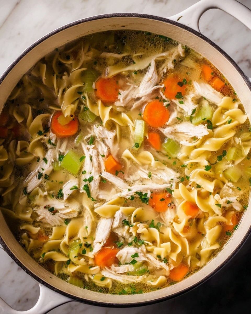 The image shows a close-up of a pot filled with chicken noodle soup. The soup has four main visible layers: a clear broth at the bottom, yellow curly egg noodles floating in the broth, soft orange carrot slices and light green celery pieces scattered through the noodles, and shredded white chicken pieces on top. Small green herbs are sprinkled evenly over the soup, adding a fresh touch. Steam rises from the pot, showing the soup is hot. The pot is white and sits on a white marbled surface. photo taken with an iphone --ar 4:5 --v 7