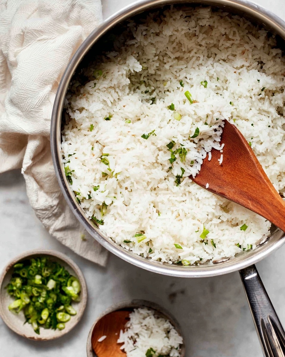 A large pot filled with cooked white rice that has small green herb pieces mixed in, creating tiny specks of green throughout. A wooden spoon rests inside the pot, lifting some rice. The pot's handle is in the foreground, and the pot sits on a white marbled surface. Nearby, there is a white cloth napkin crumpled on the surface and two small bowls holding chopped green herbs or vegetables, one with a wooden spoon. Photo taken with an iphone --ar 4:5 --v 7