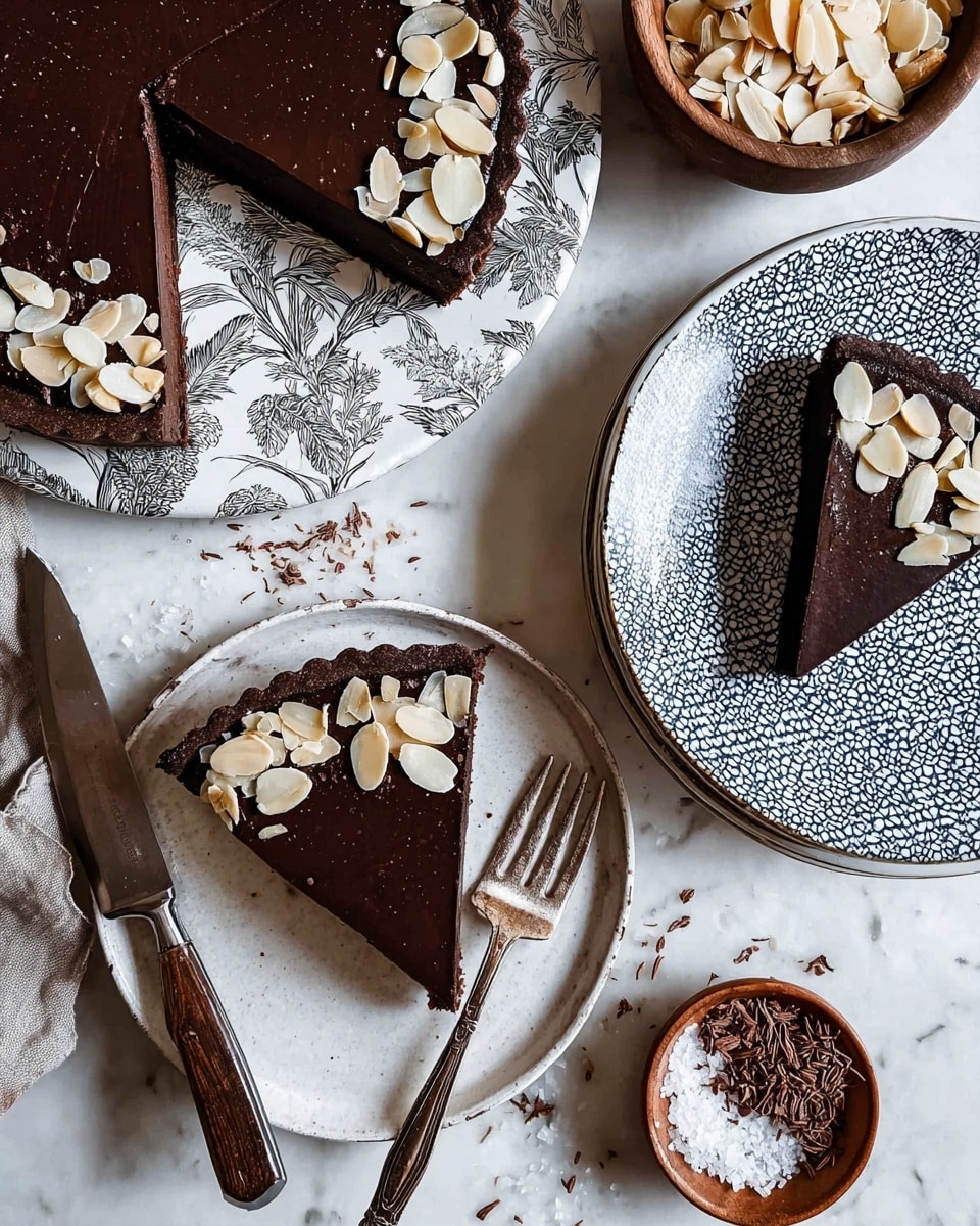 A slice of dark brown chocolate tart with a smooth surface is placed near the top center of a white plate with gray leafy patterns. The tart slice is decorated with light cream-colored thin almond slices on one edge. A tarnished silver fork lies on the plate to the right of the tart slice. Below, a white plate with blue geometric patterns holds another dark brown tart slice topped with slivered almonds at the top right. At the bottom center, a round white plate contains a chocolate tart with several slices, topped with scattered almond slivers, and a dark wooden-handled knife rests on the plate’s right side. Small bowls surround the plates: the top right has cocoa shavings on a white marbled surface, the bottom left has coarse salt in a wooden bowl, and the left middle has more almond slivers. The background is a white marbled surface. Photo taken with an iphone --ar 4:5 --v 7