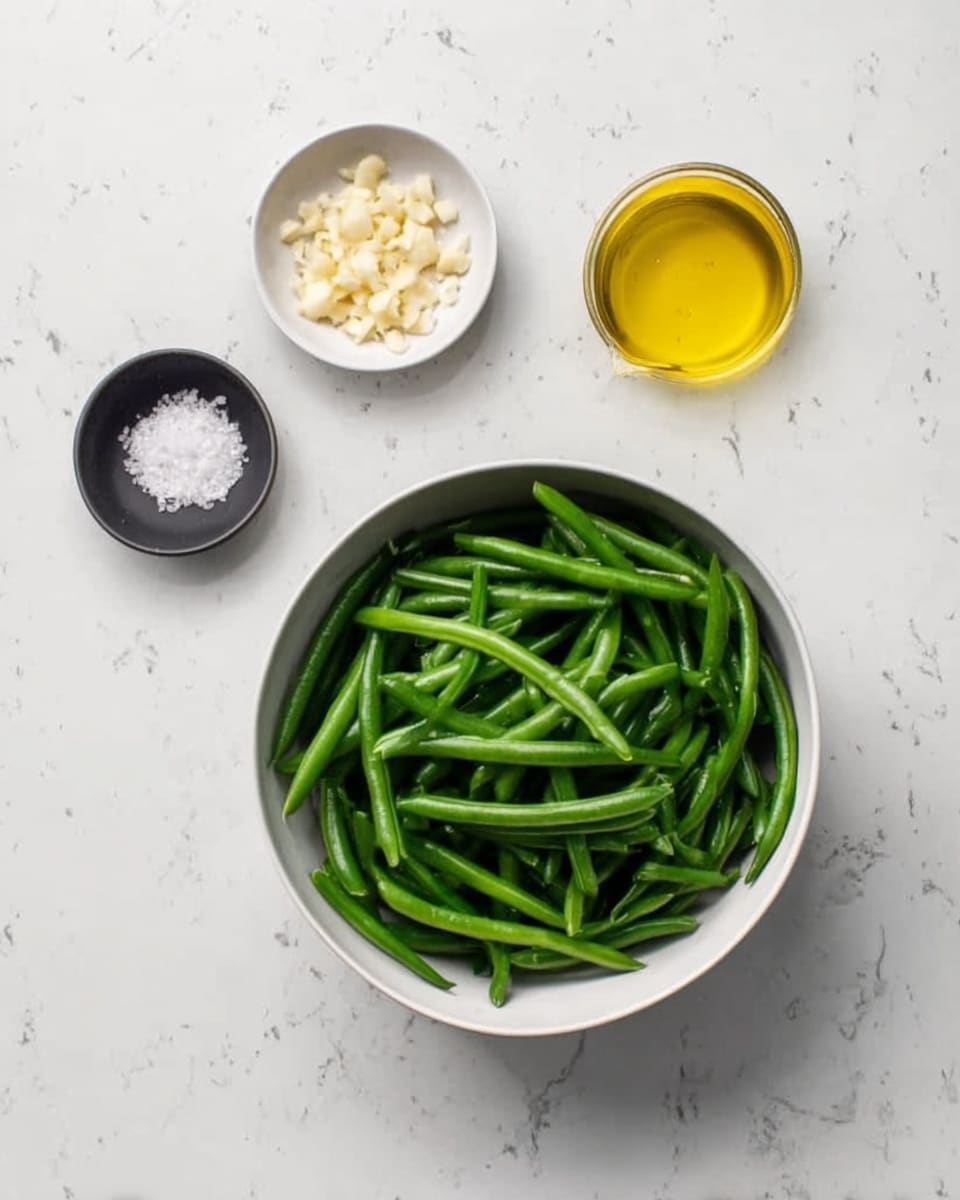 A white bowl filled with fresh, bright green beans is placed on a white marbled surface. Next to the bowl, there is a small black dish with finely chopped light beige garlic, and another small white bowl containing white coarse salt. Above these, there is a small glass container with golden yellow olive oil. Everything is arranged neatly with clear color contrasts: the green beans are smooth and shiny, the garlic looks finely textured, the salt appears coarse, and the oil is glossy. photo taken with an iphone --ar 4:5 --v 7