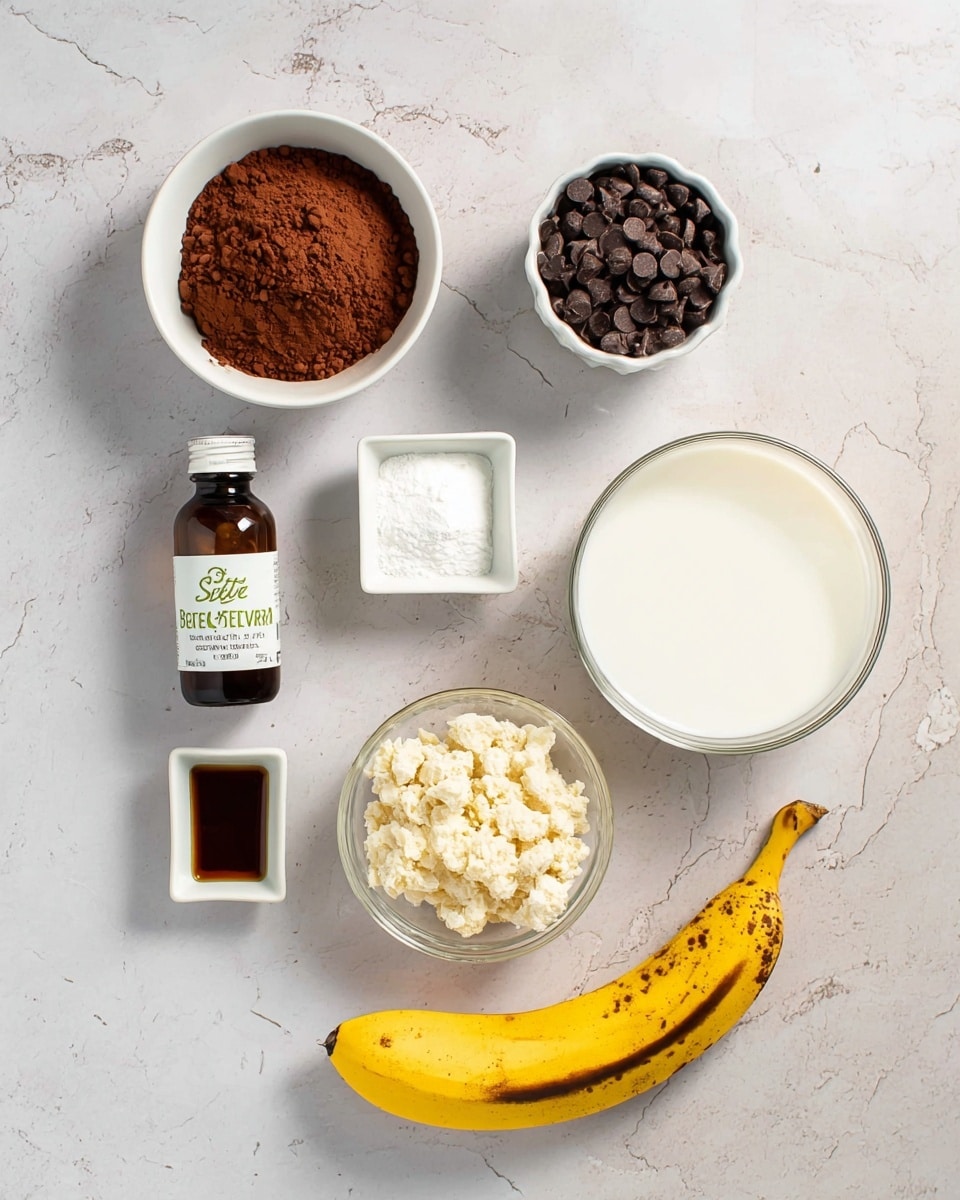 A top view of several ingredients arranged on a white marbled surface: top left is a white bowl filled with brown cocoa powder, next to it on the right is a smaller white ramekin with dark chocolate chips. Below the two, in the center, is a small white square dish holding a white powdery ingredient. On the far right, there is a larger clear glass bowl filled with white milk. Below the milk, there is a white bowl filled with a crumbly, light beige substance. In the bottom left corner, there is a dark brown bottle labeled