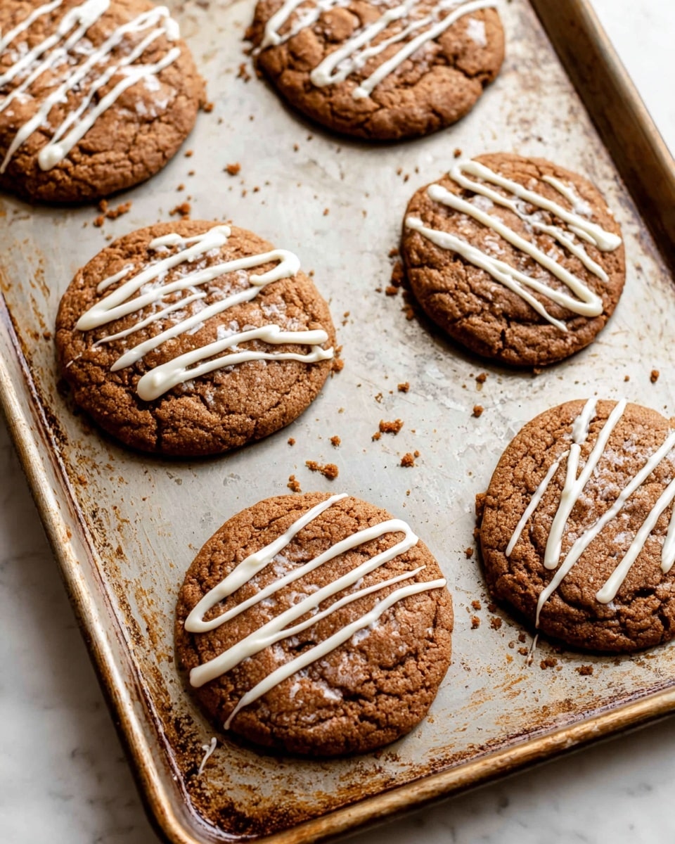 The image shows a baking sheet with five large brown cookies, each topped with three thin, wavy white icing lines that run from one side to the other. The cookies are slightly rough in texture with some small cracks and scattered crumbs around them on the metal sheet, which has a worn look with patches of browning. The cookies are spaced out unevenly on the sheet, placed on a white marbled surface. photo taken with an iphone --ar 4:5 --v 7