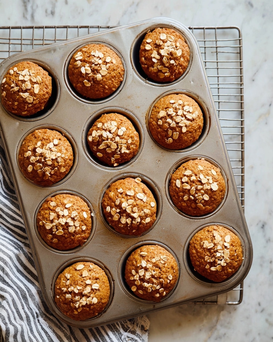 Seven brown muffins topped with small light oats are placed in a circle on a white plate with a raised, patterned rim. The plate sits on a round wooden board, which is on top of a copper wire rack, all set against a white marbled surface. In the top right corner, a white scalloped plate holds a muffin split in two, revealing a soft, airy inside, along with a small piece of biscuit. Next to it is a brown ceramic cup with white leaf patterns, filled with a dark liquid. A folded cloth with orange, blue, and cream stripes is partially visible at the bottom left. Photo taken with an iphone --ar 4:5 --v 7