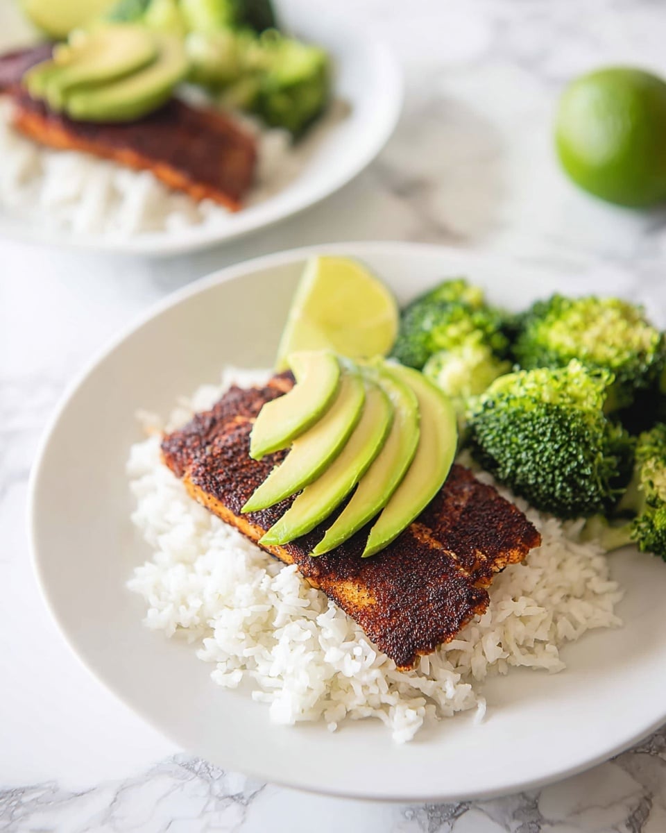 The dish shows a white plate with three main layers: at the bottom, there is a bed of fluffy white rice, on top of the rice is a piece of dark, seasoned cooked fish with a crispy texture, and on the fish are three slices of smooth, light green avocado placed in a slight fan shape. To the right side of the plate are bright green, tender broccoli florets, and above them is a lime wedge adding a fresh touch. In the background, there is another similar plate and a whole lime on a white marbled surface. photo taken with an iphone --ar 4:5 --v 7