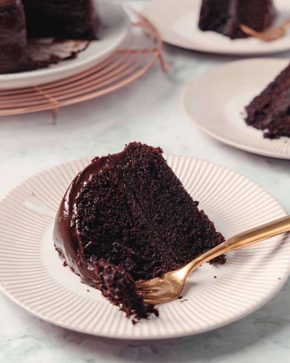 A single slice of rich dark chocolate cake is placed on a white plate with a ridged edge. The cake shows two layers with a smooth, shiny dark chocolate frosting between them and coating the sides. The top layer looks soft and crumbly, and some crumbs have fallen onto the plate. A gold fork rests on the cake, partially inserted into the lower layer. In the background, more slices of the same cake are visible on white plates on a white marbled texture surface. photo taken with an iphone --ar 4:5 --v 7