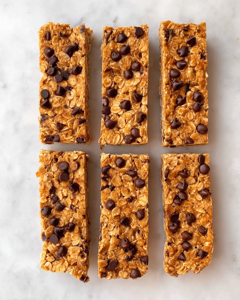 Five rectangular granola bars are placed in a vertical line on a white marbled texture. Each bar has a golden brown base made mostly of oats and peanut butter, with many small, dark brown chocolate chips spread evenly on the surface. The texture is rough and chunky, showing bits of oats and peanut pieces within the bars. Photo taken with an iphone --ar 4:5 --v 7