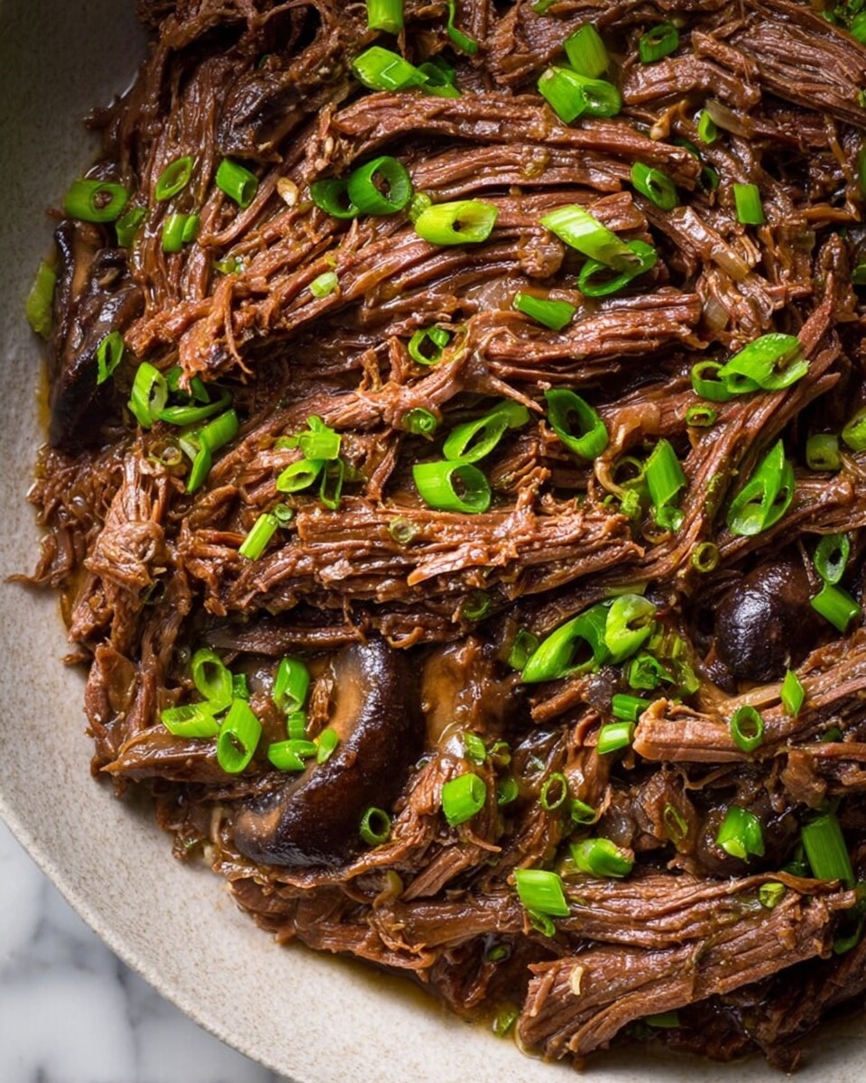 The dish shows shredded brown beef layers with a moist and tender texture, mixed with dark brown cooked mushroom slices. Small bright green chopped scallions are sprinkled evenly on top, adding fresh color contrasts. The layers of beef appear stringy but soft, overlapping naturally to create a textured look. The whole dish sits on a white marbled surface. Photo taken with an iphone --ar 4:5 --v 7