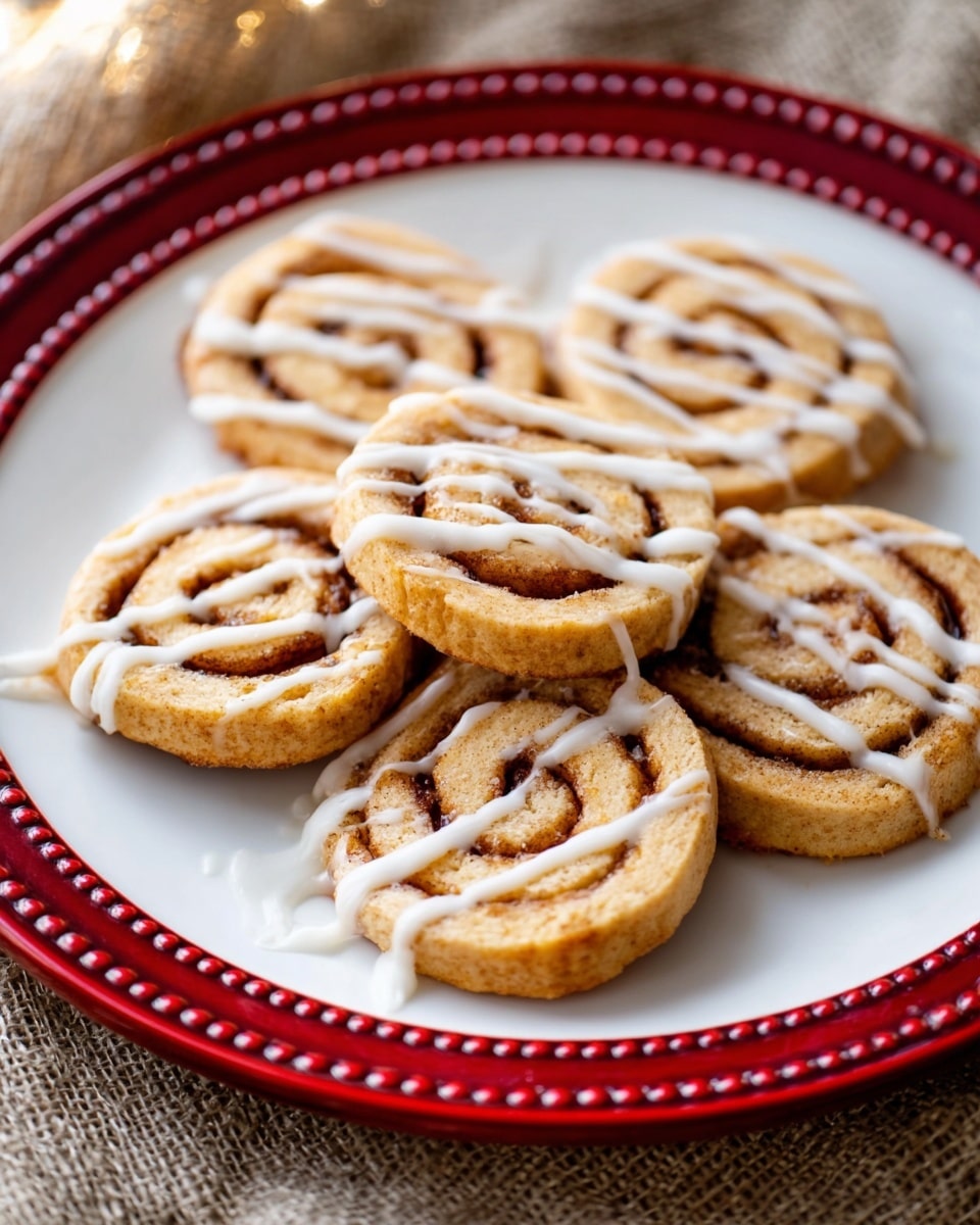 Seven cinnamon roll cookies sit on a white plate with a red decorative edge and raised dot border. Each cookie is light golden brown with a visible spiral of cinnamon filling. The cookies are topped with thin white drizzle of icing, unevenly spread across their surfaces. The plate is placed on a beige fabric with textured weave, and the background is softly blurred. photo taken with an iphone --ar 4:5 --v 7