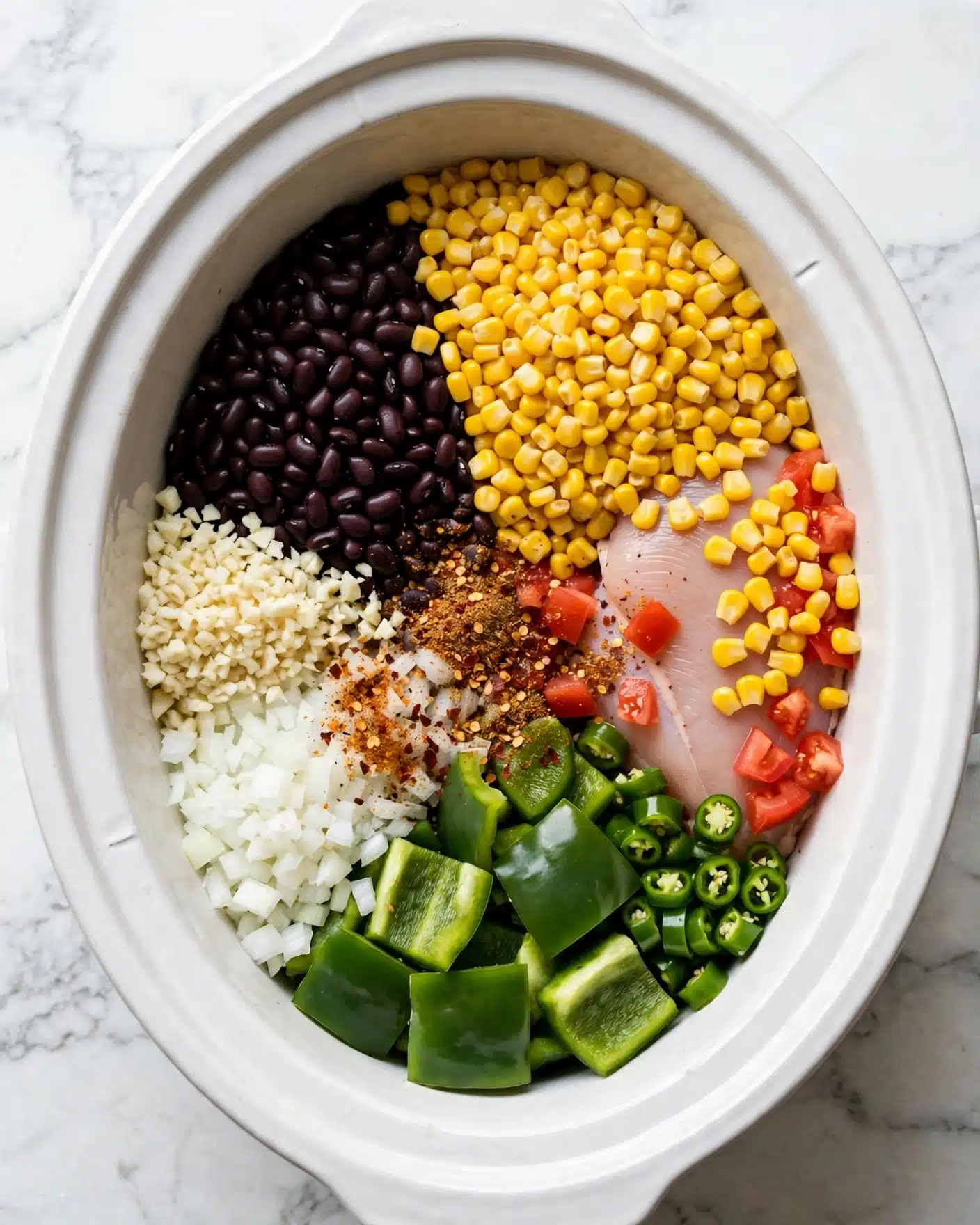My Favorite Slow Cooker Chicken Chili Recipe 4 Inside a white oval slow cooker, there are seven layers arranged around the center. On the top right, bright yellow corn kernels cover a large area. To the left of the corn, dark black beans fill a large section. Below the beans, finely chopped white garlic sits next to chopped white onions. Moving right from the onions, large pieces of green bell peppers fill the bottom right section, with smaller pieces of green chili peppers beside them. A raw piece of chicken with a pale pink color is partly covered by the corn and diced red tomatoes on the far right. In the center, a mix of brown and red spices is sprinkled on top of the onions and chicken. The whole cooker rests on a white marbled surface. Photo taken with an iphone --ar 4:5 --v 7