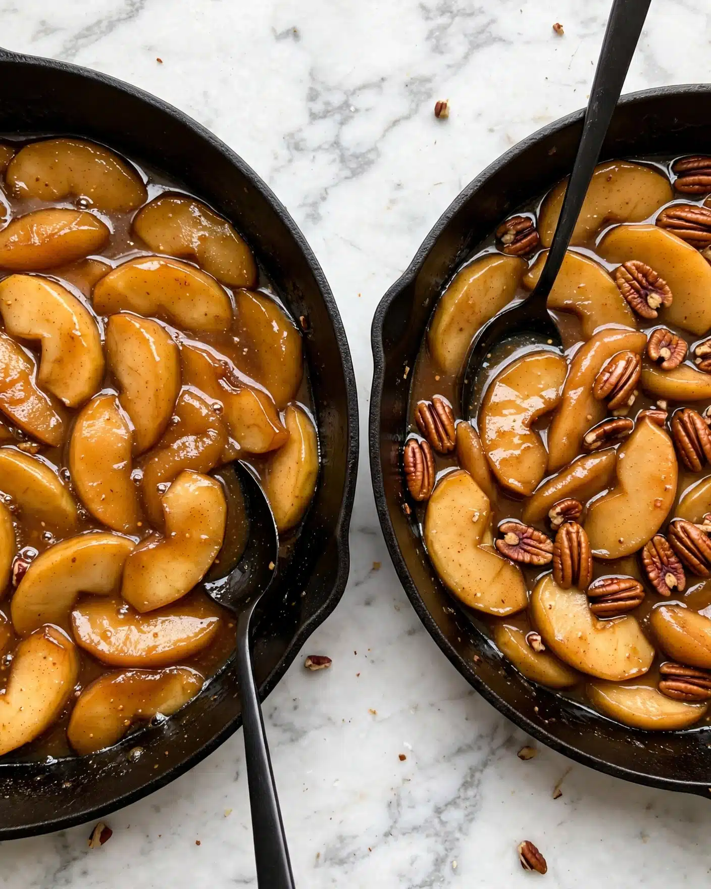 Baked Apple Cider French Toast Recipe 4 The image shows two black pans on a white marbled surface, each filled with cooked apple slices. In the left pan, there are many golden-brown apple slices cooked in a shiny syrup with a black spoon resting on the side. In the right pan, similar golden apple slices are mixed with shiny brown pecans scattered throughout and the same black spoon is partially submerged in the syrup. The apple slices have a soft texture with light spice specks visible on them. The syrup has a rich amber color giving everything a warm, glossy look. photo taken with an iphone --ar 4:5 --v 7
