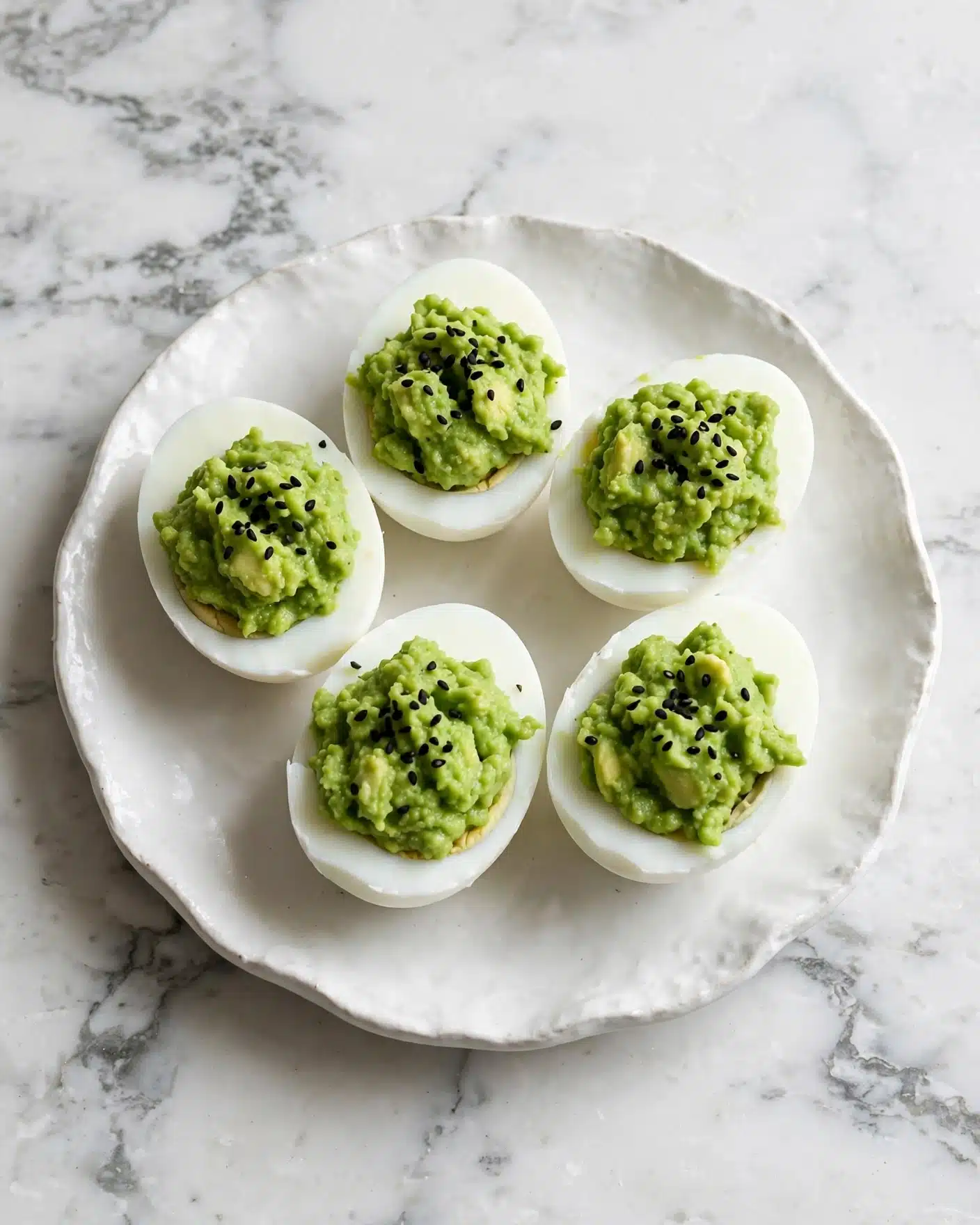 Five white egg halves are arranged on a round white plate with a slightly wavy edge. Each egg half has a smooth white outer layer, and the center is filled with a bright green mashed mixture that has a soft, slightly chunky texture. Small black seeds are sprinkled on top of the green filling, adding contrast. The plate sits on a white marbled surface. photo taken with an iphone --ar 4:5 --v 7