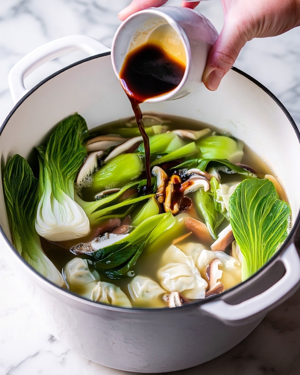A white pot filled with clear broth soup containing bright green bok choy with crisp leaves and pale stalks sitting on top, alongside cream-colored dumplings with soft, smooth folds. Light brown shiitake mushrooms with curved slices float gently in the soup. A woman's hand is pouring a dark brown sauce from a small white cup into the center of the pot. The background features a white marbled surface. photo taken with an iphone --ar 4:5 --v 7